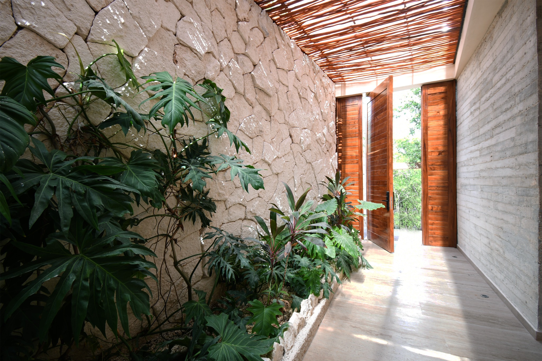 Pasillo de Zakktal con muros de piedra, vegetación tropical y celosía de madera.